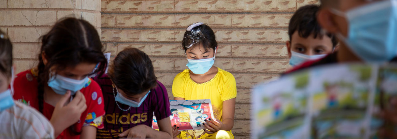 Children sit down with leaflets in an explosive ordnance risk education session