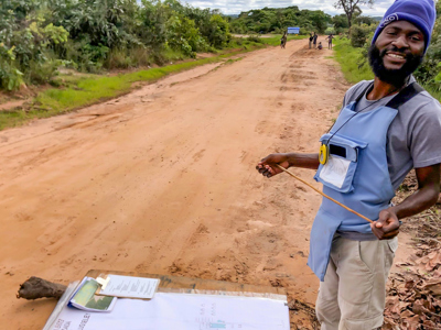 A man in HALO's PPE stands at the side of a dusty road with a large sheet of paper on the ground