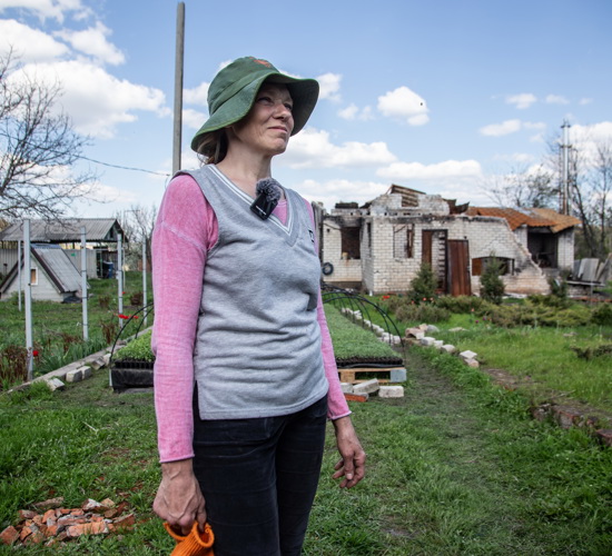 Natalia, a resident of Kharkiv, stands in her backyard with destroyed homes behind her