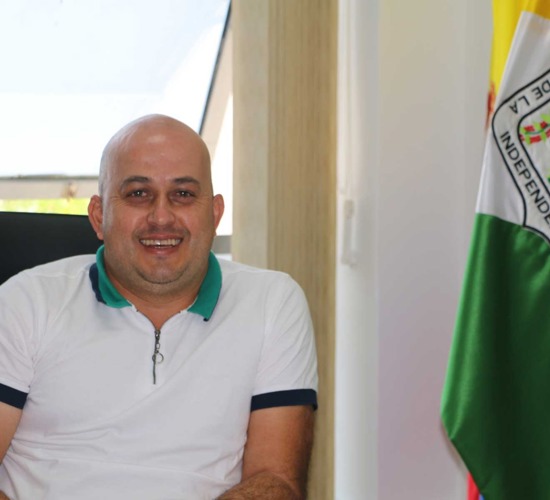 The mayor of Campamento smiles whilst sitting in a room with a flag 