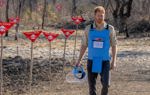 Prince Harry walks through a minefield in Angola, wearing PPE and holding a visor next to red danger signs