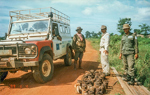 Three men stand next to a vehicle on a sandy track next to a large pile of mines