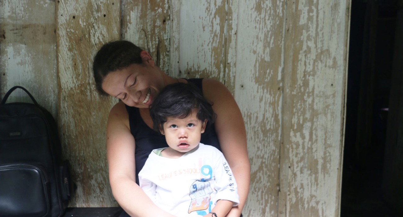 A woman sits and smiles with her baby on her lap