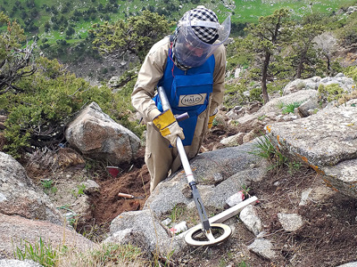 A deminer using their metal detector above rocks and soil
