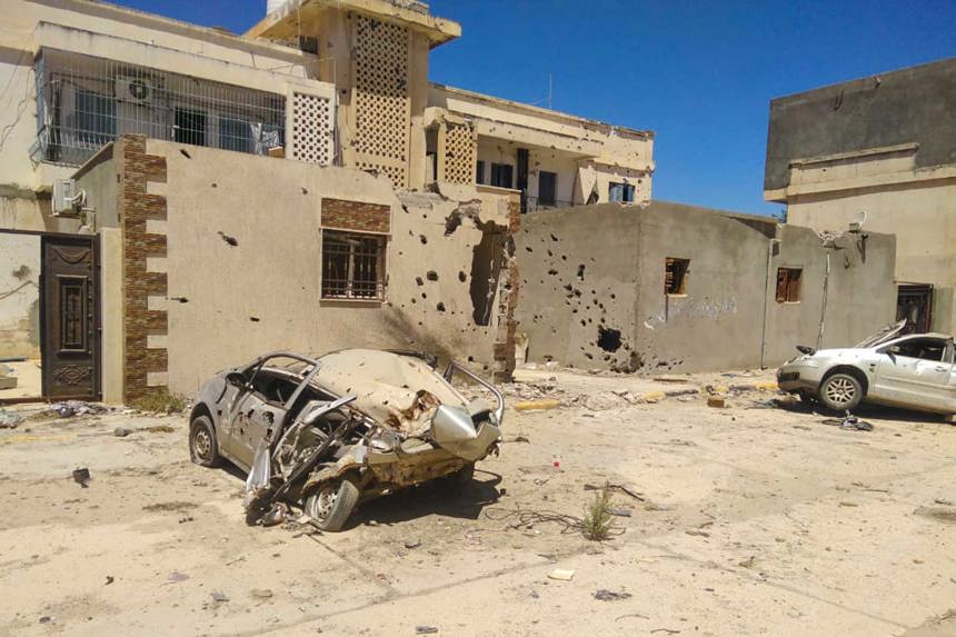 Damaged vehicles sit outside damaged buildings in Tripoli