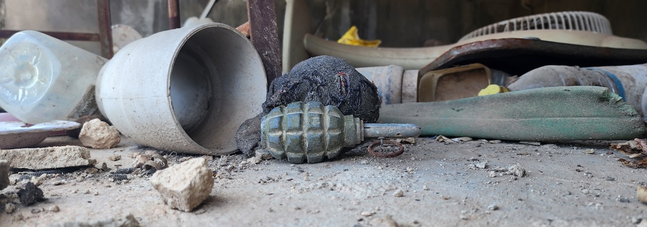 A grenade on the floor amongst rubble and household belongings in Syria