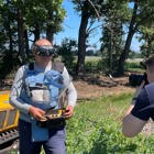 Журналісти фотографують демінера в захисному спорядженні з пультом керування від машини для дистанційної зрізки рослинності Robocut на фоні цієї машини біля лісопосадки