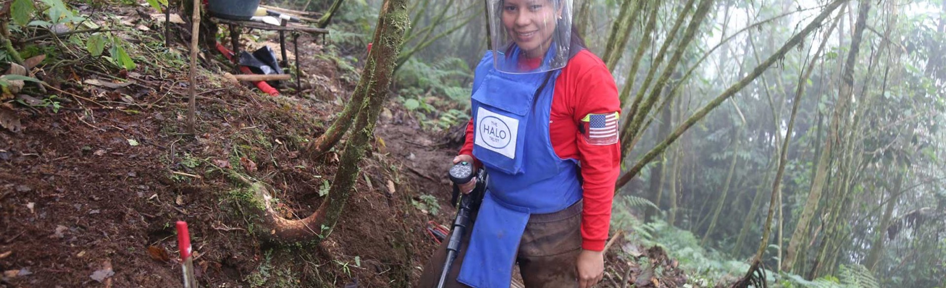 A female deminer poses with her metal detector whilst wearing PPE