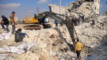 Men stand around an excavator in Al-Atareb city being used for rubble removal