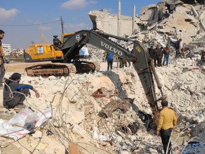 Men stand around an excavator in Al-Atareb city being used for rubble removal