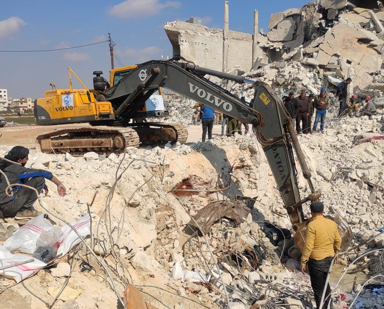 Men stand around an excavator in Al-Atareb city being used for rubble removal