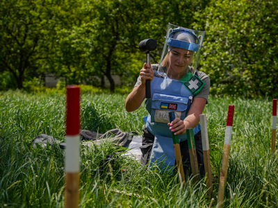 A deminer wearing protective gear hammers mine marking sticks into the grass
