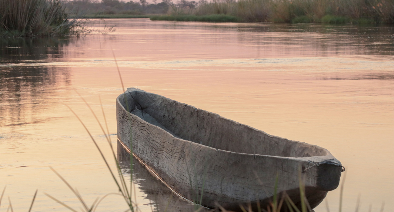 A carved wooden canoe on the Cuito river during sunset