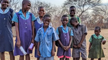 A group of children in school uniform smile in a rural area